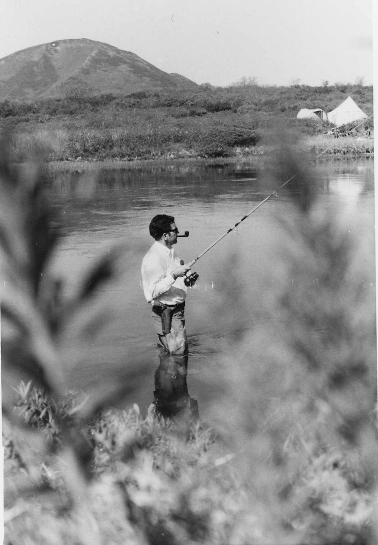 Sen. Ted Stevens sports a handgun strapped to his side, and his pipe as he fishes in an unknown place. His glasses and pipe place this in the 1970's. No print in file - don't know provenance of image. Stevens Foundation